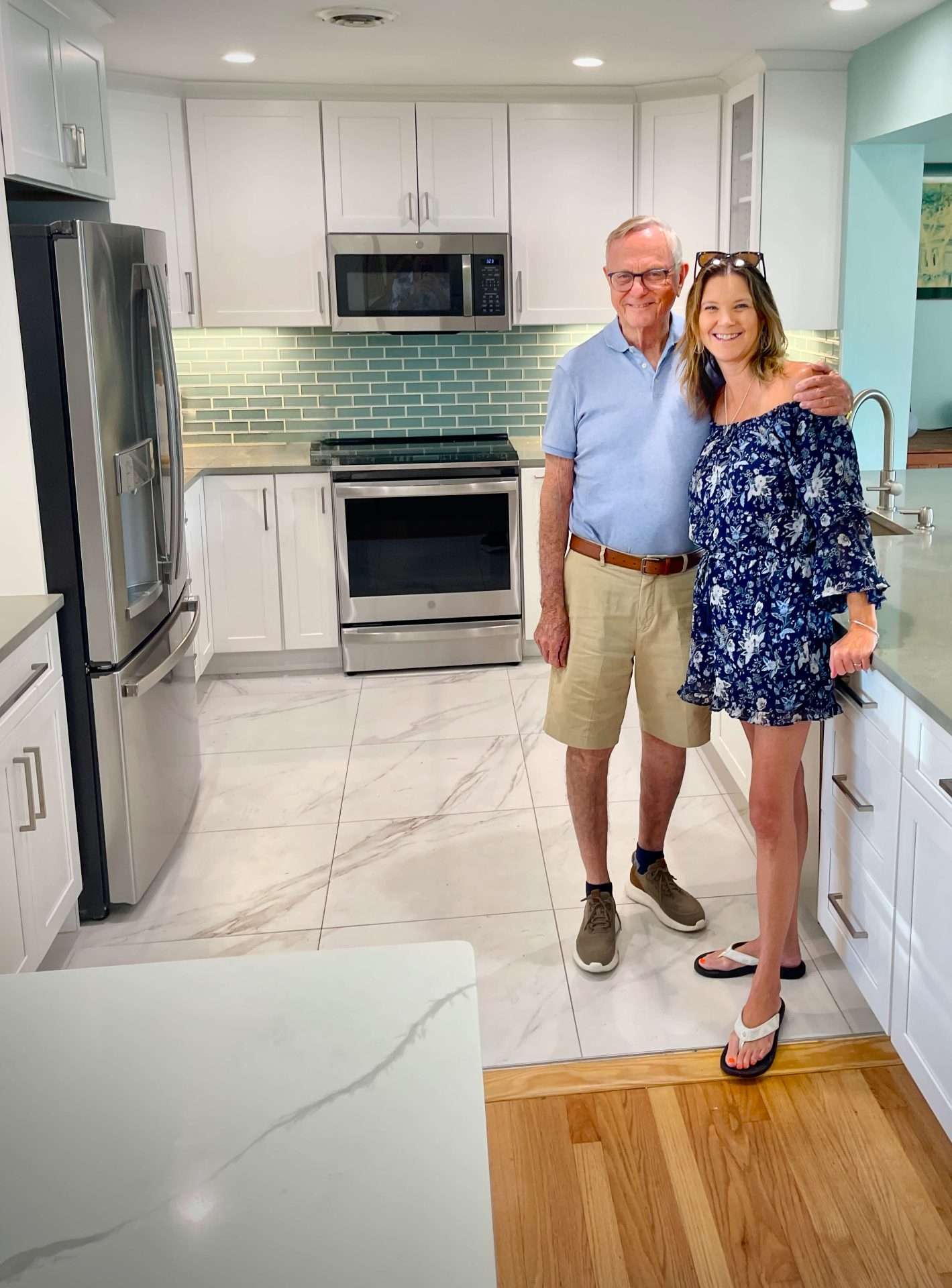 Ormond-Beach-kitchen-designer-Kacie Kacie Lee, lead designer at Timeless Kitchen & Bath Remodeling, with an Ormond Beach homeowner in a newly remodeled kitchen featuring white shaker cabinets, gray quartz countertops, and a soft blue tile backsplash