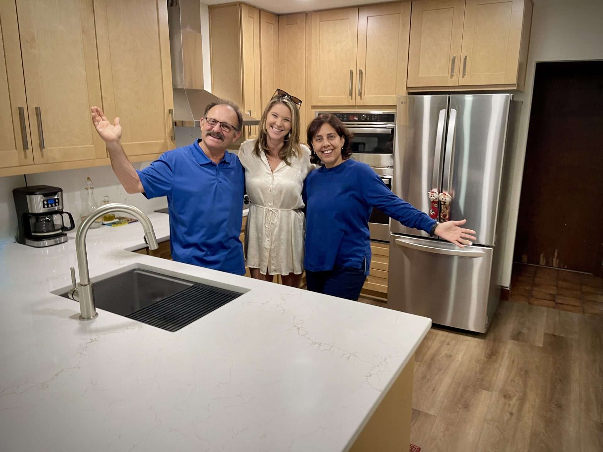 Homeowners standing with lead designer Kacie Lee in their newly remodeled Ormond Beach kitchen featuring light wood cabinetry, quartz countertops, and a clean, modern island layout.